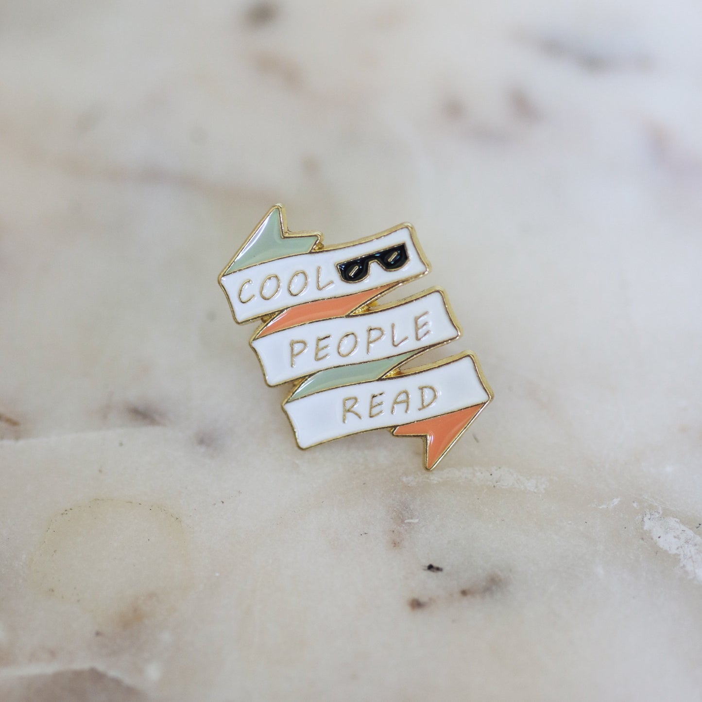 A pin shaped like a white, pink, and mint banner with sunglasses and the phrase Cool People Read. From Copper Crow Swag Market's Book Pins collection