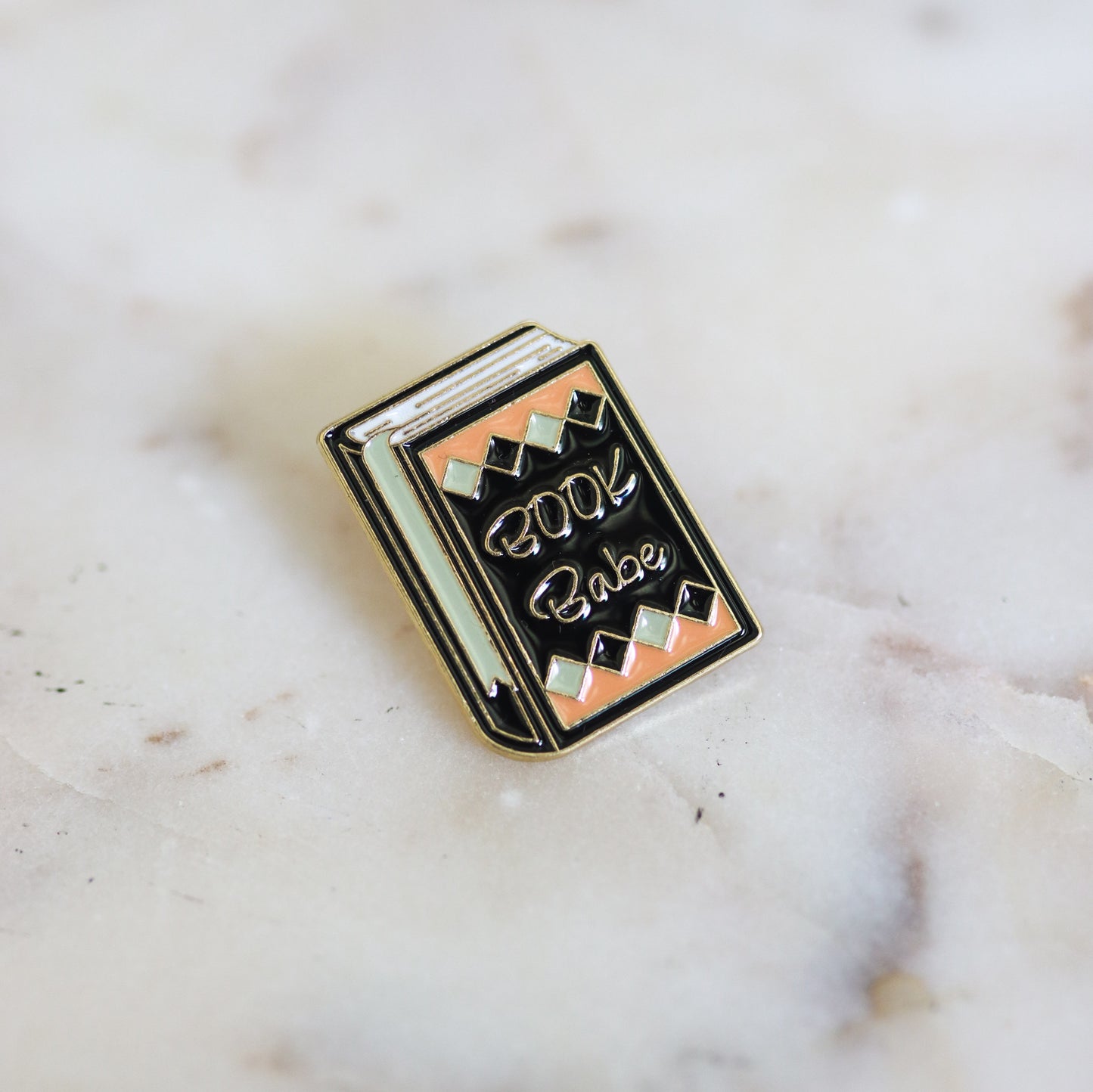 A black, pink, and mint colored enamel book pin with the phrase Book Babe on the cover. From Copper Crow Swag Market's Book Pins collection