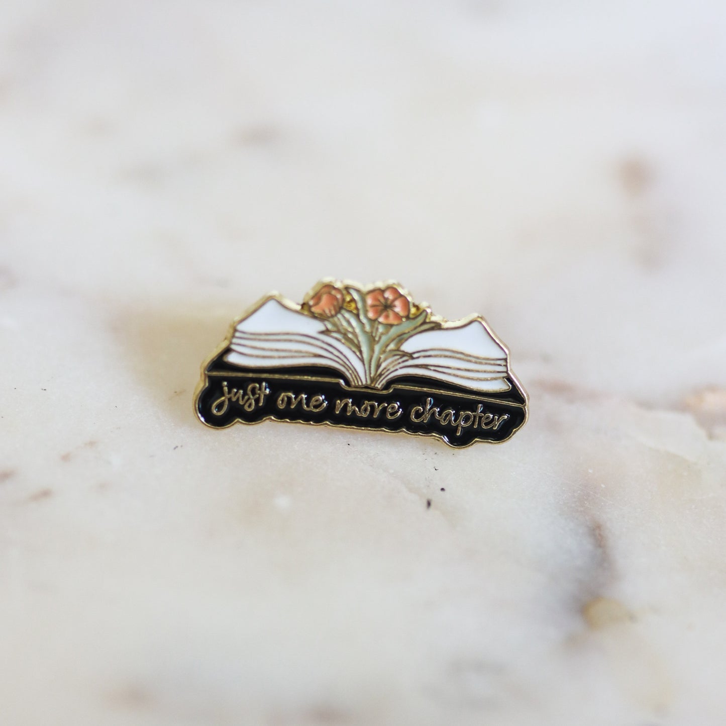An open book with flowers, enamel book pin, with the phrase Just One More Chapter. From Copper Crow Swag Market's Book Pins collection