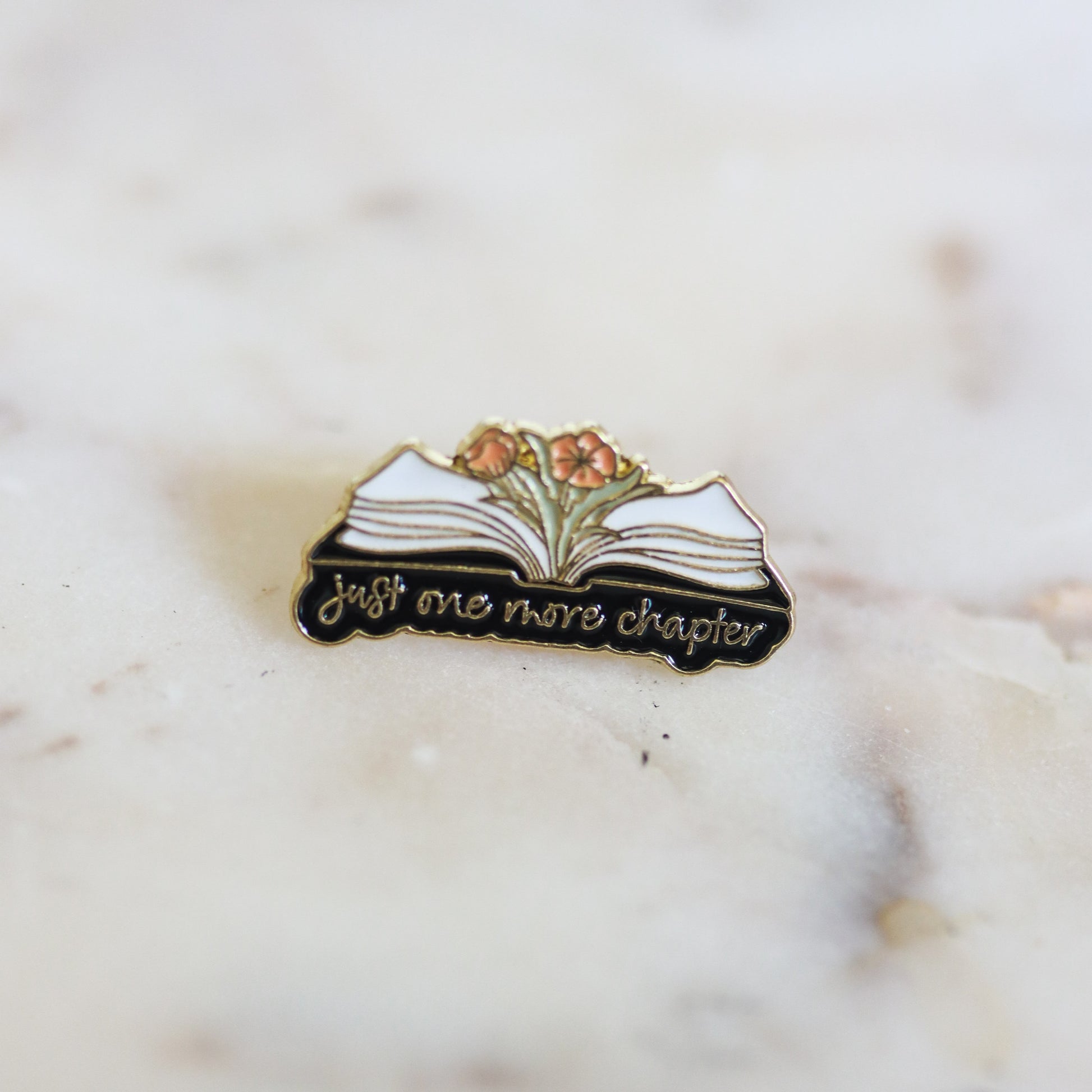 An open book with flowers, enamel book pin, with the phrase Just One More Chapter. From Copper Crow Swag Market's Book Pins collection