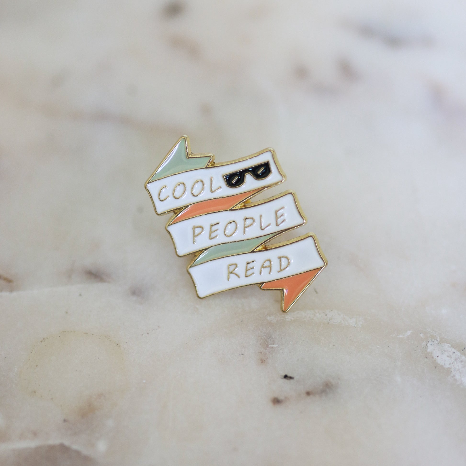 A pin shaped like a white, pink, and mint banner with sunglasses and the phrase Cool People Read. From Copper Crow Swag Market's Book Pins collection